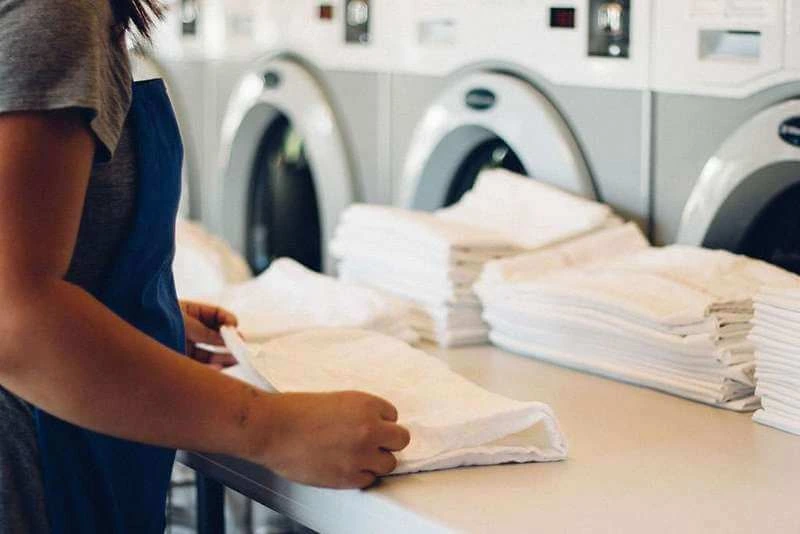 Person folding clean white laundry in a laundromat setting. Representing Difference Between Laundry and Dry Cleaning.